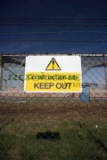 construction-site-keep-out-sign-on-chain-link-fence-surrounding-redevelopment-building-site-with-old-factory-in-the-background