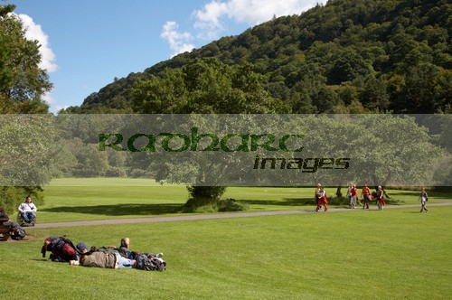 tourists-lying-on-the-grass-others-walking-along-pathway-beneath-the-hills-on-open-ground-in-grounds-glenalough-monastic-site