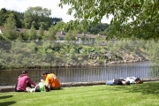 tourists-lie-on-the-grass-soaking-up-the-sunshine-in-avoca-village-county-wicklow-overlooking-the-river